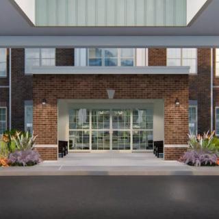 A modern building entrance with a brick facade and glass doors, featuring well-maintained landscaping.