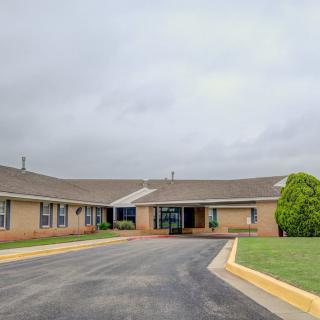 A single-story brick building with a driveway and landscaped surroundings under a cloudy sky.