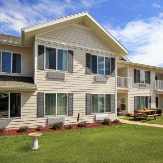 A two-story apartment building with beige siding and a well-maintained lawn on a clear day.