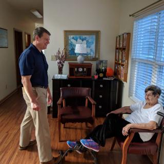 A person is sitting in a living room while another stands nearby, engaging in conversation.