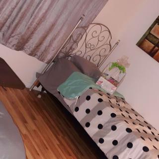 A cozy bedroom featuring a bed with a polka dot blanket and pillows, situated on a wooden floor near curtains and decorative items.
