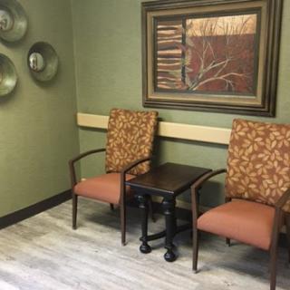 A cozy waiting area featuring two upholstered chairs and a small table, complemented by framed artwork on the wall.
