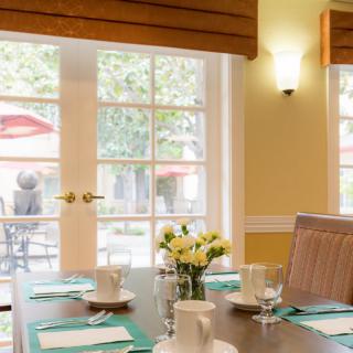 A cozy dining room with a neatly set table, featuring teacups and a vase of flowers by the window.