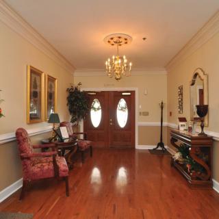 An elegant entryway featuring a chandelier, wooden flooring, and classic decor elements like decorative mirrors and furniture.