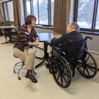 A caregiver engages in a supportive conversation with an elderly person in a wheelchair, fostering connection and care.