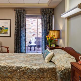 A cozy bedroom with a neatly made bed, decorative pillows, and a bedside lamp next to a nightstand.