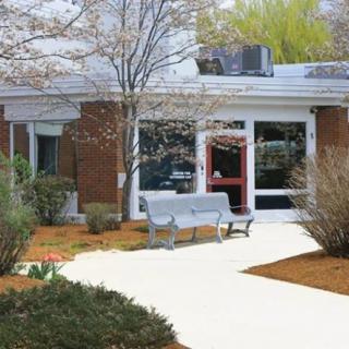 Front entrance of a school building with surrounding landscaping and a bench.
