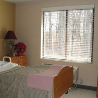 A hospital room with a bed positioned near a large window with blinds.