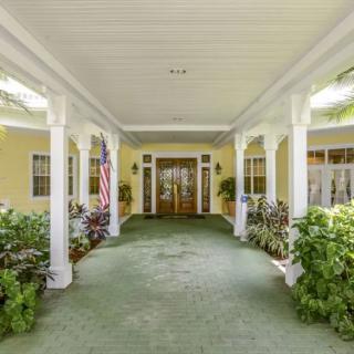 A spacious entryway with white columns, lush greenery, and a green carpet leading to double wooden doors.