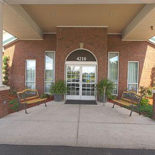 The entrance of a brick building features benches, plants, and an arched doorway.