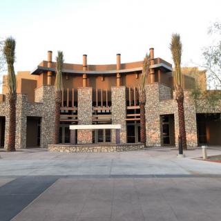 A modern building with a stone facade and palm trees at the entrance.