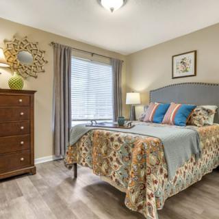A cozy bedroom with patterned bedding, a wooden dresser, and a window with curtains.
