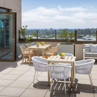 A rooftop terrace with tables and chairs overlooks the cityscape on a sunny day.
