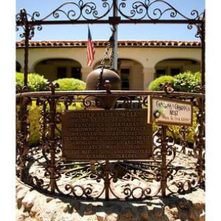 A historic site marked with a plaque, surrounded by an ornate iron gate, with a building and garden in the background.