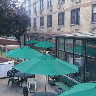 A serene outdoor seating area with green umbrellas and tables, situated next to a building.