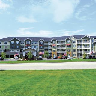 A multi-story residential apartment complex with a well-maintained lawn and clear skies.