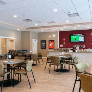 A modern cafe with neatly arranged tables and chairs, featuring a television on the wall.