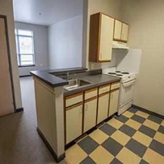 A small apartment kitchen with checkered flooring and simple cabinetry.