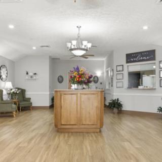 A modern reception area featuring wooden flooring, a central desk with a floral arrangement, and a waiting area with seating.