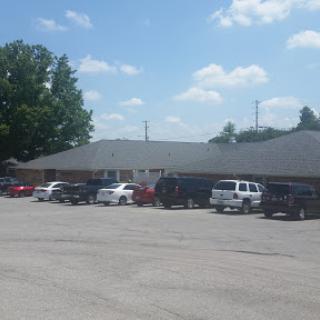 A view of a commercial building with multiple vehicles parked in front under a partly cloudy sky.