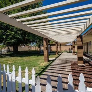 A backyard featuring a pergola and white picket fence under a clear blue sky.