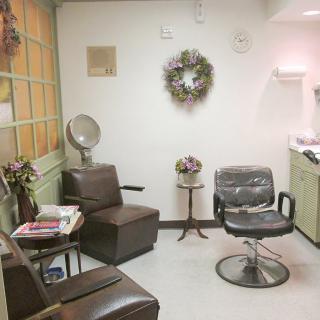 A cozy hair salon with comfortable seating, a styling chair, and decorative details such as a wreath and flowers.