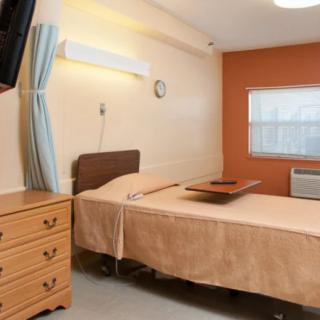 A clean and simple hospital room with a bed, dresser, and window.