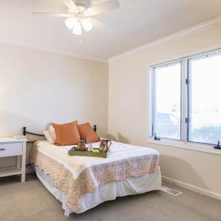 A cozy bedroom with a neatly made bed, large window, and soft lighting.