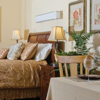 A cozy bedroom with elegant decor, featuring a wooden bed, decorative pillows, bedside lamps, and framed artwork on the walls.