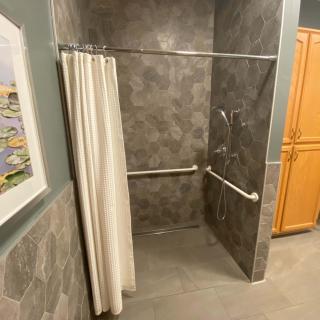 An accessible bathroom shower with grab bars and a curtain.