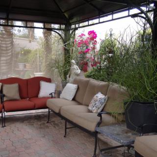 A cozy outdoor seating area under a gazebo, surrounded by lush plants and flowers.