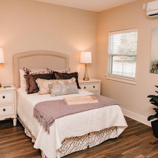 A cozy bedroom with a neatly made bed, flanked by two nightstands and lamps, featuring warm decor.