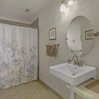A modern bathroom with a pedestal sink, oval mirror, and floral shower curtain.