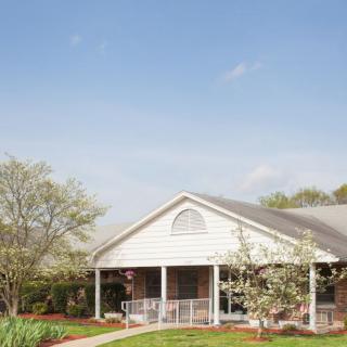 A residential house with a white porch surrounded by trees and a clear sky.