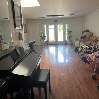 A spacious living room featuring a piano and hardwood flooring, with large glass doors allowing natural light to fill the space.
