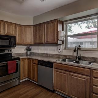 A modern kitchen with wooden cabinets and stainless steel appliances, including an electric stove, microwave, and dishwasher.
