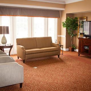 A cozy living room with warm tones, featuring a sofa, chairs, and a large window with curtains.
