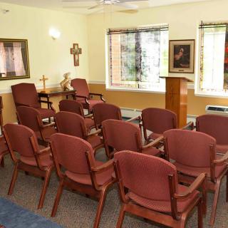 A small chapel with rows of chairs, a podium, and a cross on the wall.