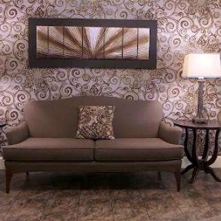 A cozy living room setup featuring a stylish sofa, decorative pillow, elegant lamp, and patterned wallpaper.