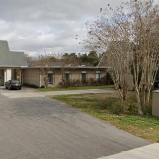 A suburban building with a driveway and surrounding trees under a cloudy sky.