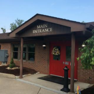 A brick building with a red door and an awning marked 'Main Entrance'.