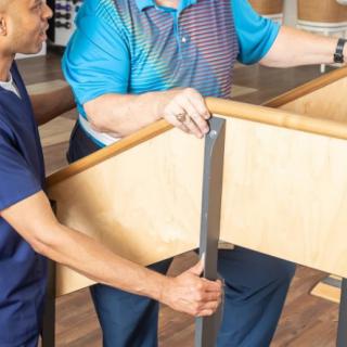 A healthcare professional assists a patient with physical therapy exercises using parallel bars.