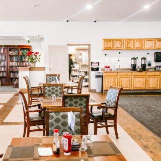 A cozy restaurant interior with neatly arranged tables and chairs, featuring a view of the kitchen area.