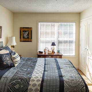 A cozy bedroom with a neatly made bed, patterned bedding, and natural light filtering through the window.