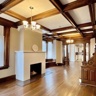 A spacious living room with hardwood floors, featuring a fireplace and ceiling beams.