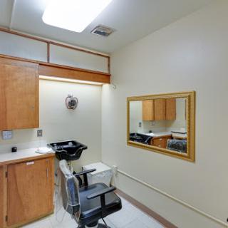 A well-lit hair salon room featuring a mirror, chair, and wooden cabinetry.