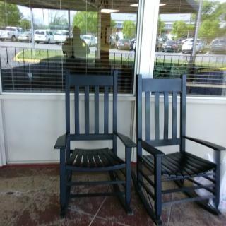 Two black rocking chairs sit on a porch in front of a window reflecting the outside view.