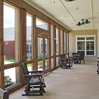 A sunlit porch with wooden rocking chairs and large windows.