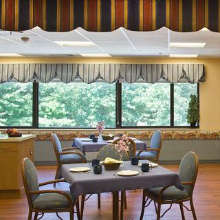A well-lit dining room with a table set for four, featuring large windows and decorative curtains.