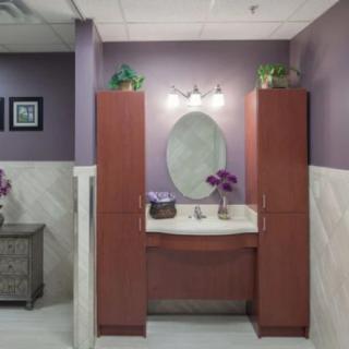 A well-decorated bathroom with purple walls, featuring a central sink and mirror framed by tall cabinets.